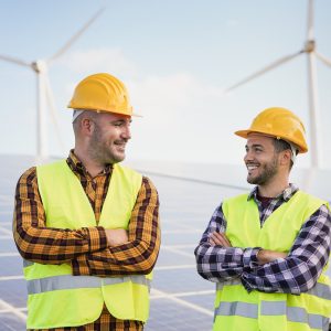 worker-men-at-solar-power-station-solar-panels-with-wind-turbines-in-background.jpg